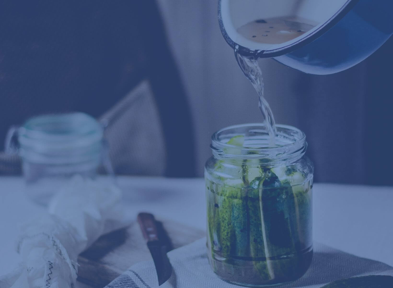 a hand pouring pickling brine from a pot into a mason jar of homemade pickles