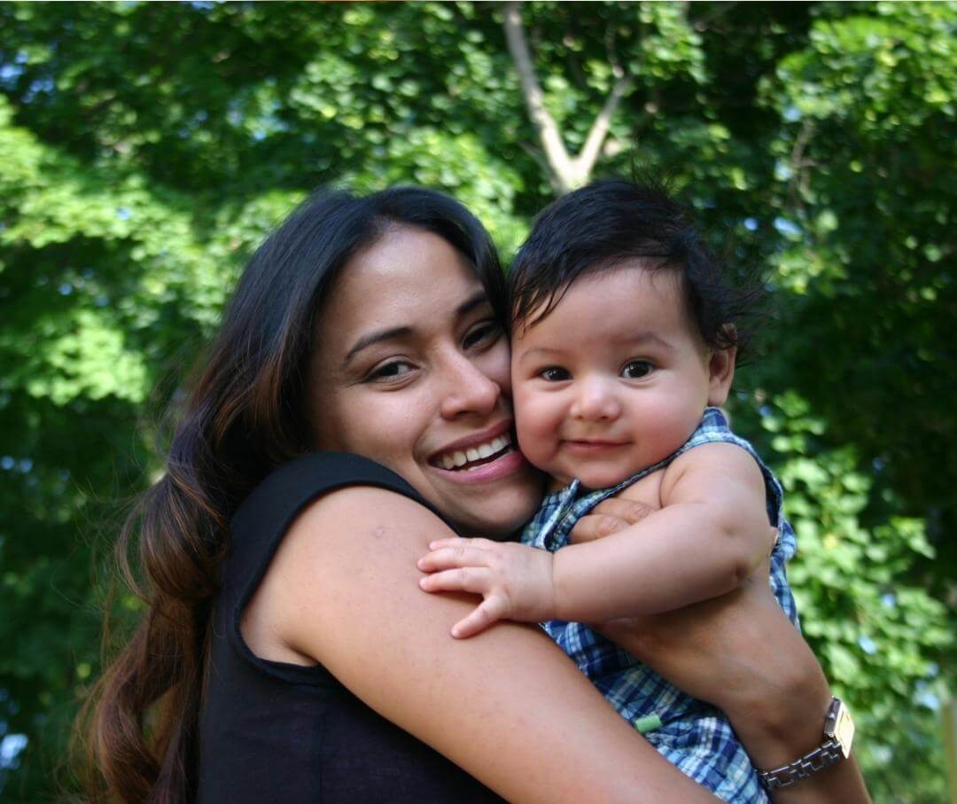 a woman cuddling her baby and smiling in a wooded area