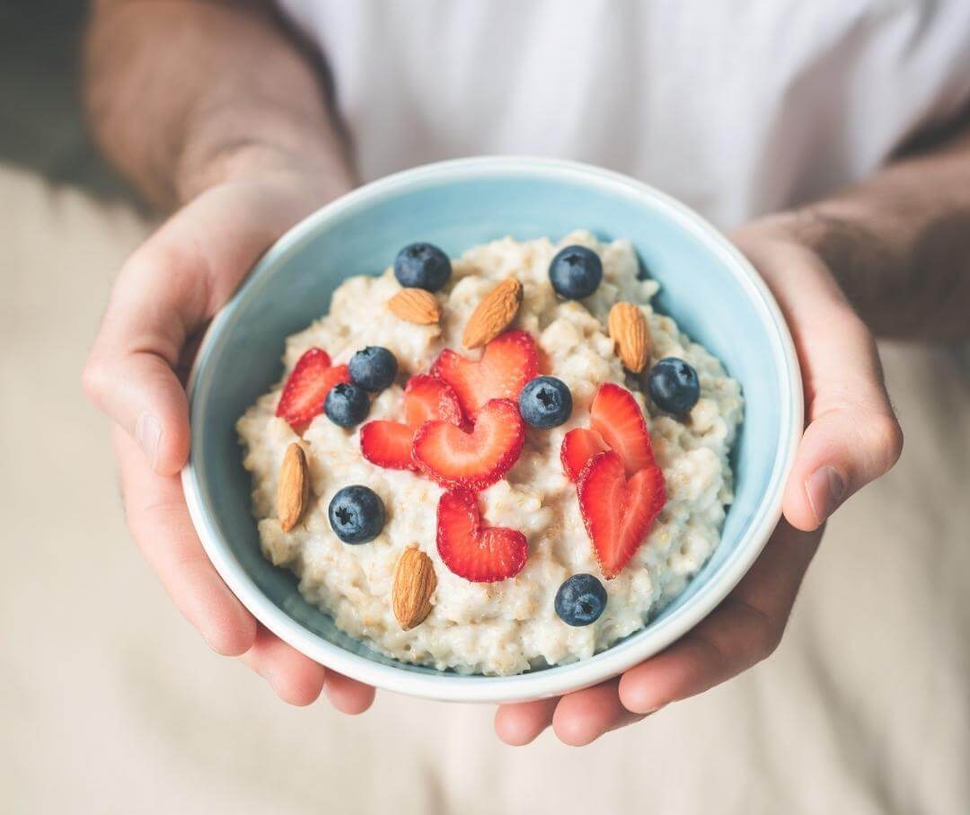 Person holding bowl of oatmeal topped with strawberries and blueberries