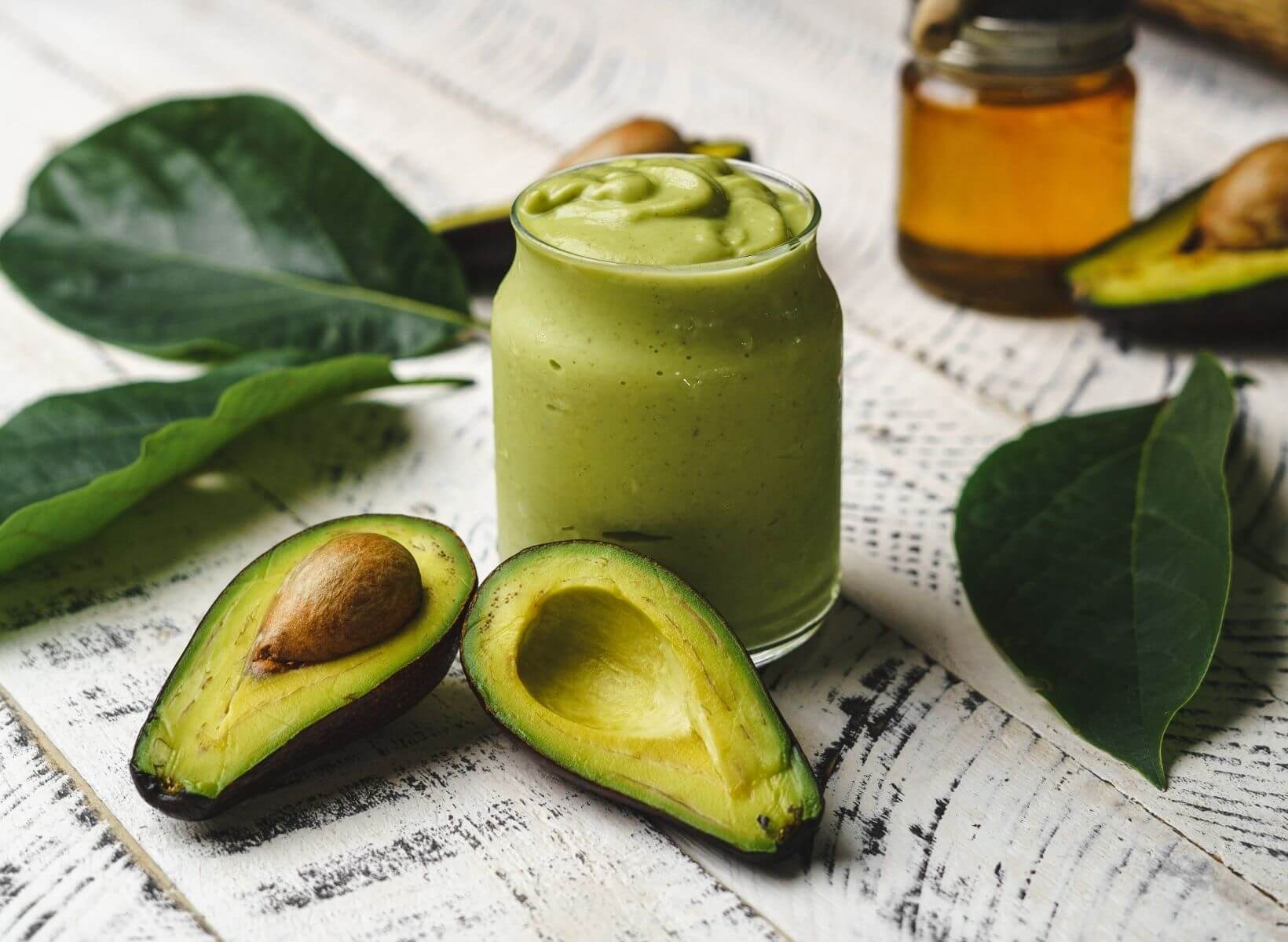 Avocado Cilantro Lime Dressing in a glass jar with green leaves and a ripe avocado cut in half around the jar