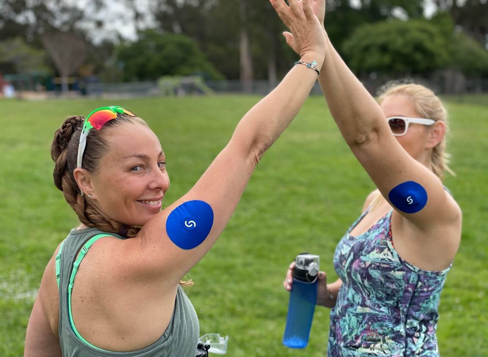 Two women wearing CGMs and Signos patches on their arms do a high five