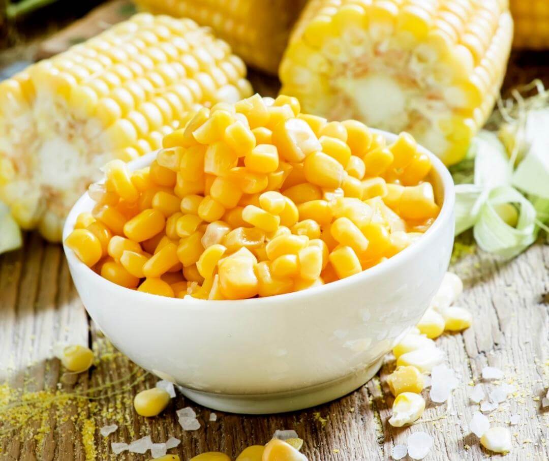 a bowl of sweet corn with corn cobs in the background