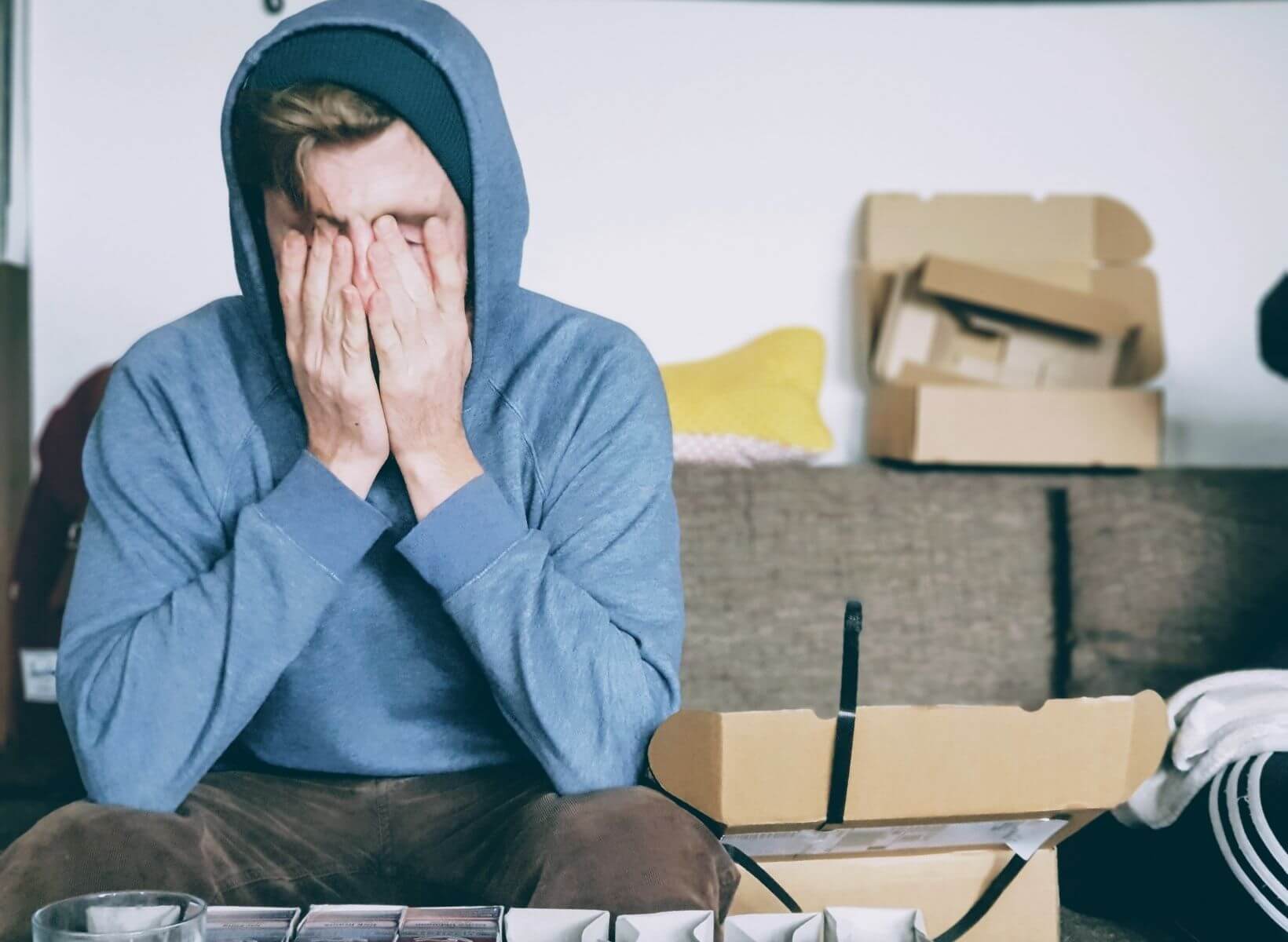 A young man sitting on a couch with his hands over his face. He's stressed, which can cause blood sugar to rise.