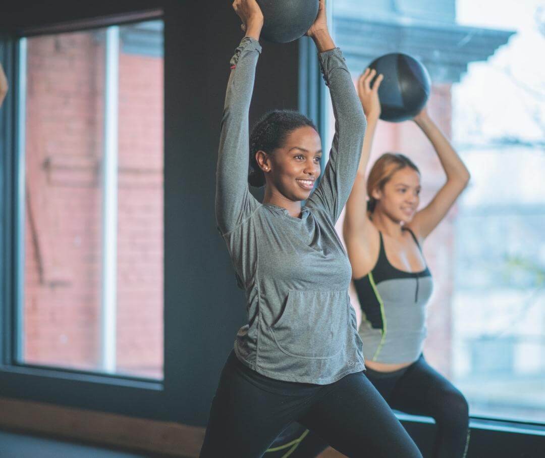 women in an exercise class holding medicine balls overhead