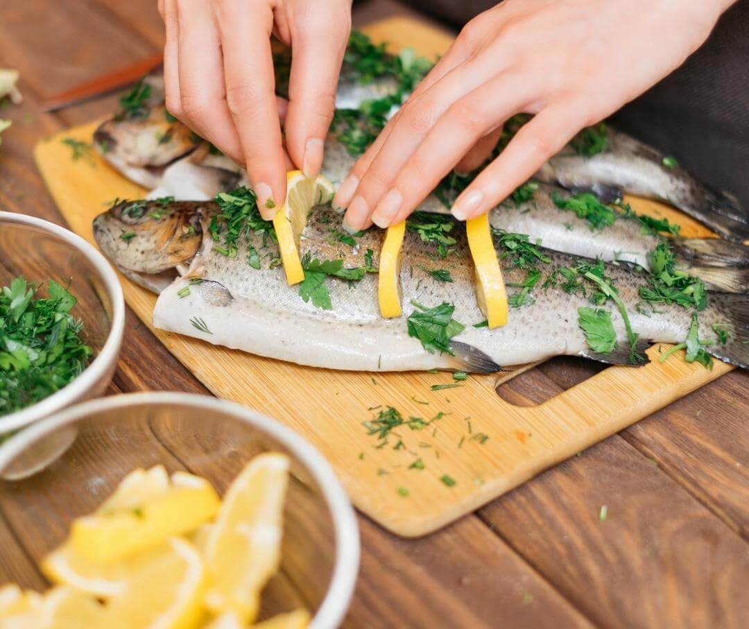 female hands preparing whole fish with lemon slices and herbs before baking