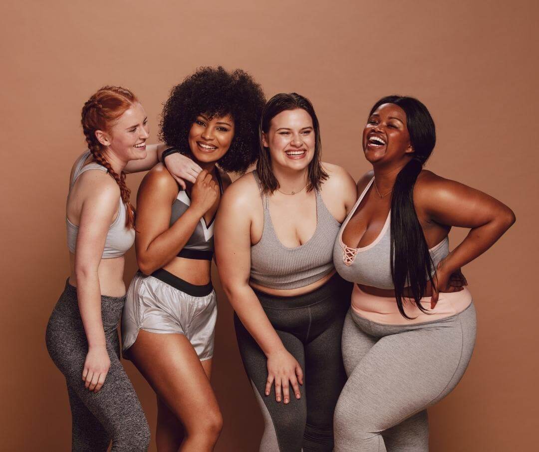 four women with different body types wearing workout clothes and smiling