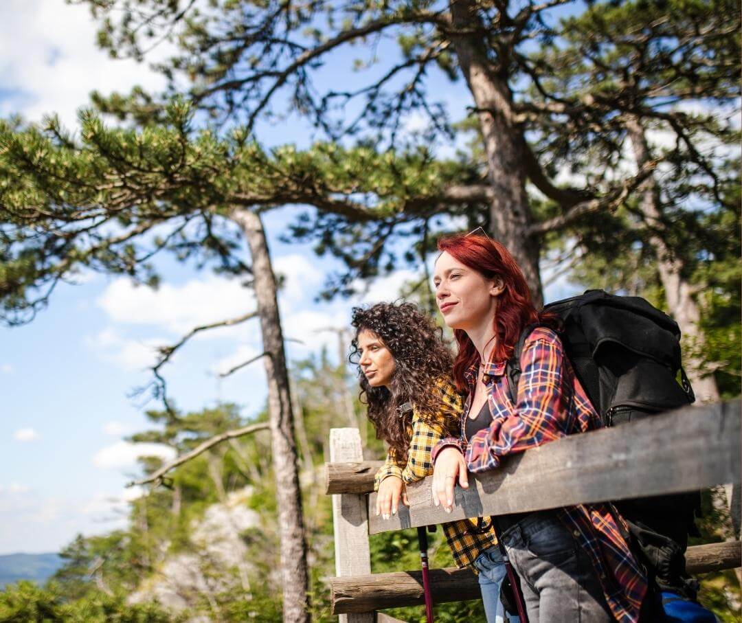 two female hikers looking out over a scenic view in the woods