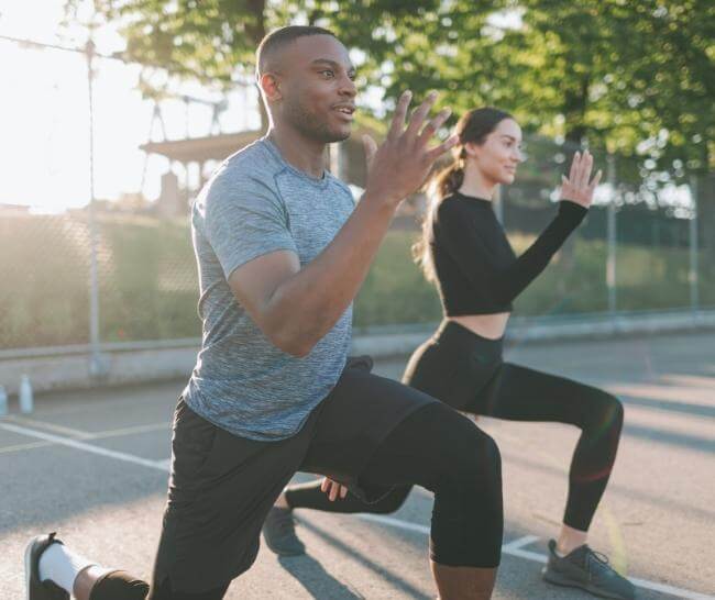 A man and woman doing lunges in a park just after sunrise