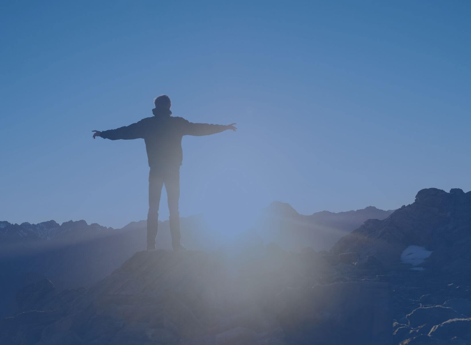 man standing on a hilltop with his arms outstretched, looking at the sunrise