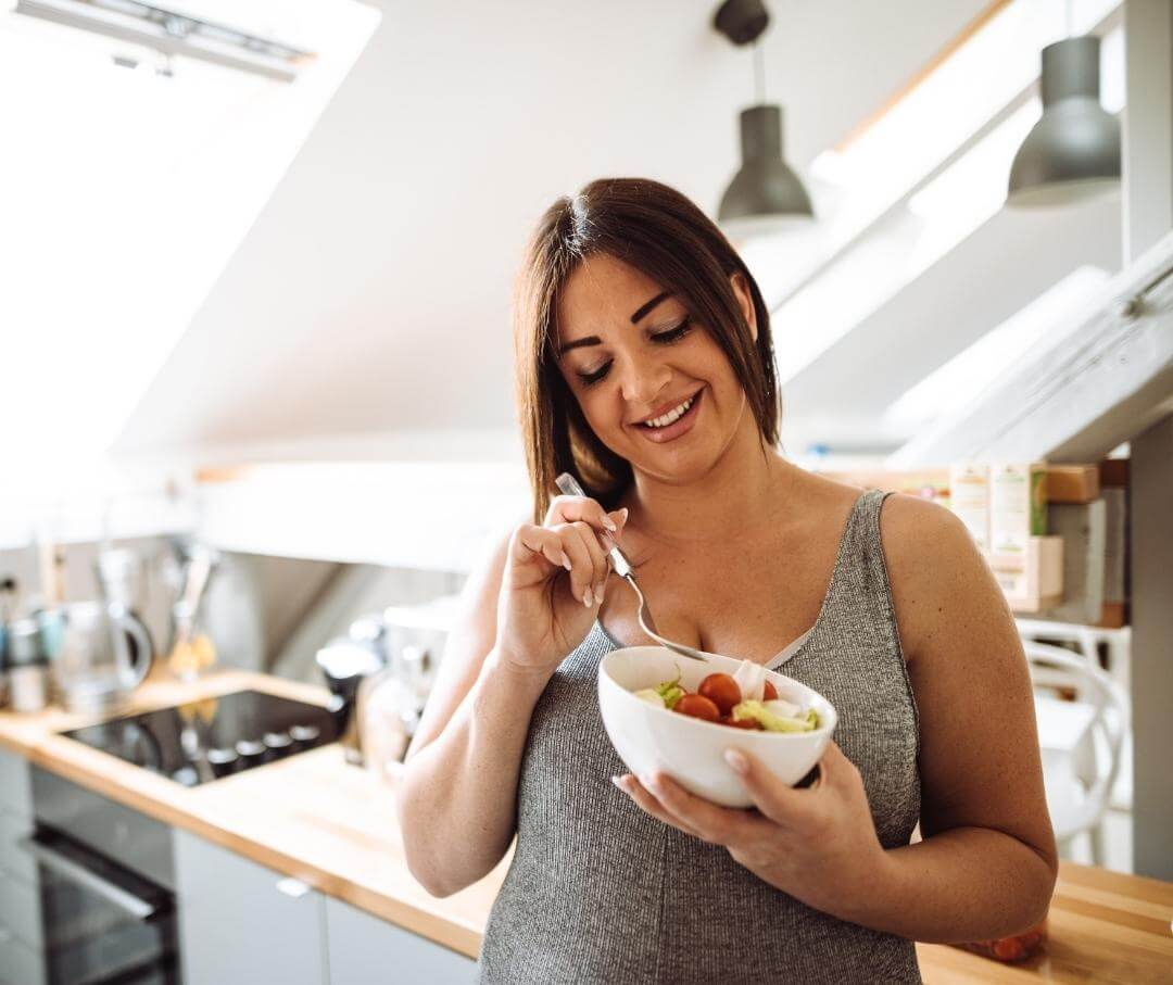 a woman eating a salad in standing up in the kitchen