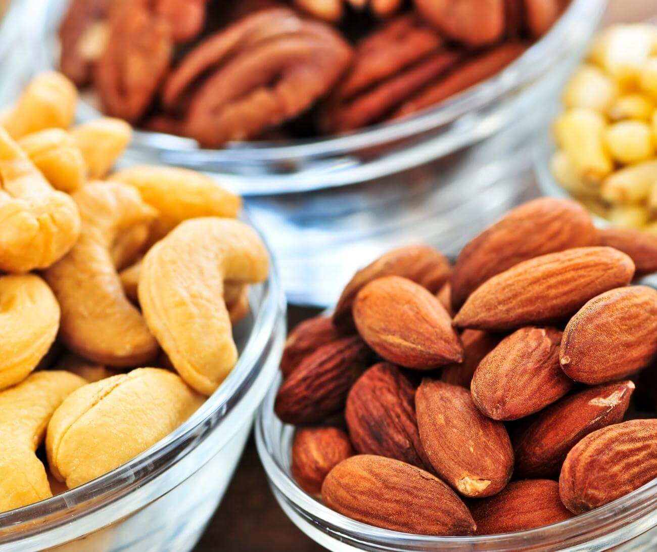 four bowls filled with nuts: cashews, almonds, pecans, and peanuts