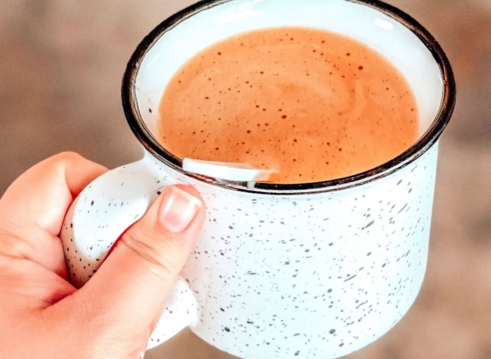 A closeup shot of a hand holding a white mug with keto coffee inside