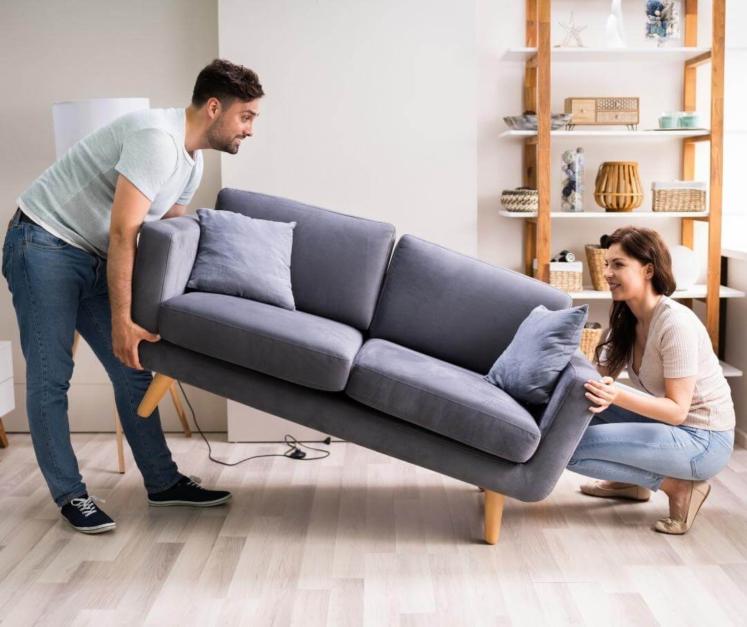 a woman and a man lifting a sofa inside a living room