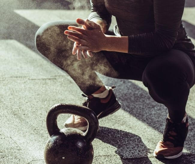 Woman putting chalk on her hands before picking up a kettlebell