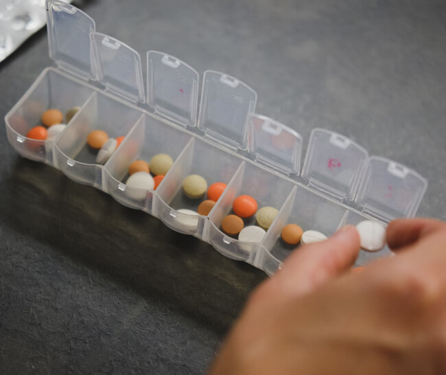 Person grabbing medication out of daily medication reminder container