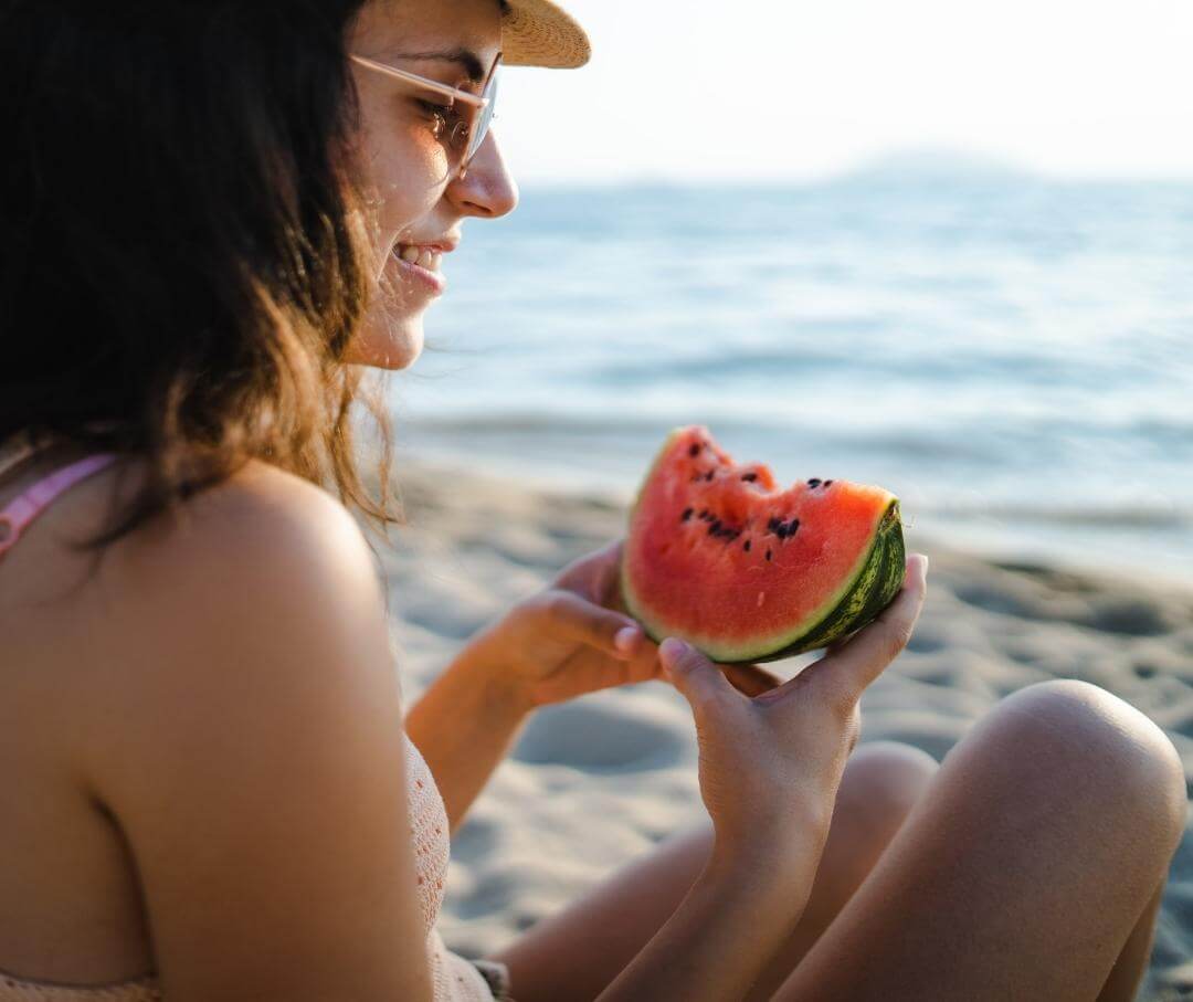 woman sitting on the beach eating watermelon with seeds