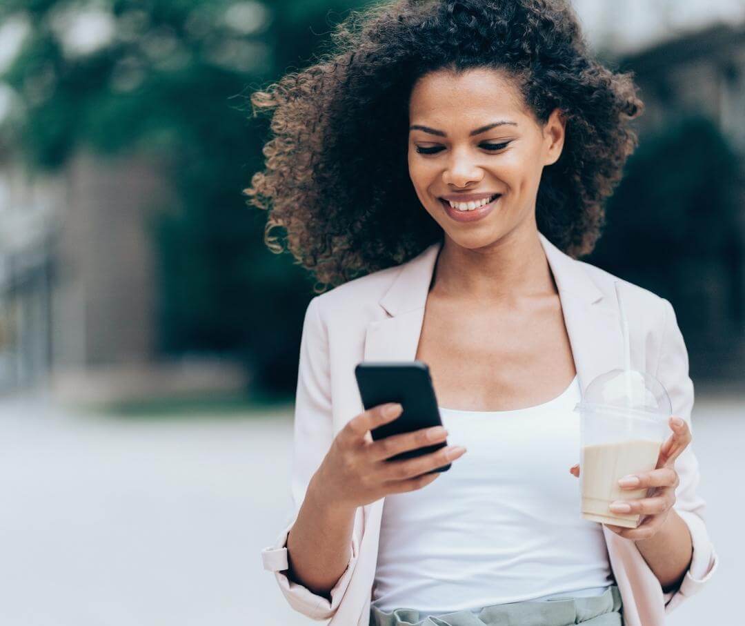 woman smiling and looking at her smartphone while walking outdoors