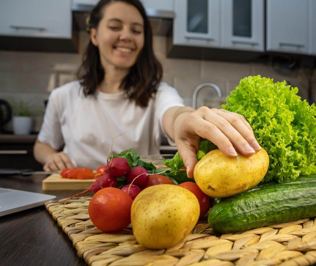 a woman reaching for a potato on a kitchen island