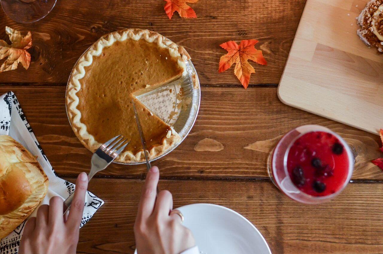 pumpkin-pie-being-cut-on-top-of-wooden-table-with-fall-leaves