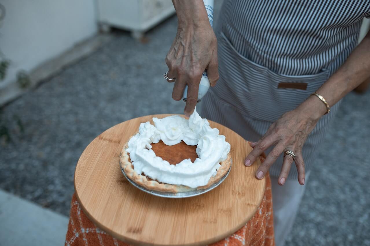 elderly-person-hans-putting-icing-on-baked-pumpkin-pie