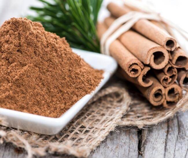 a heap of ground cinnamon on a square plate next to a bundle of rolled cinnamon sticks