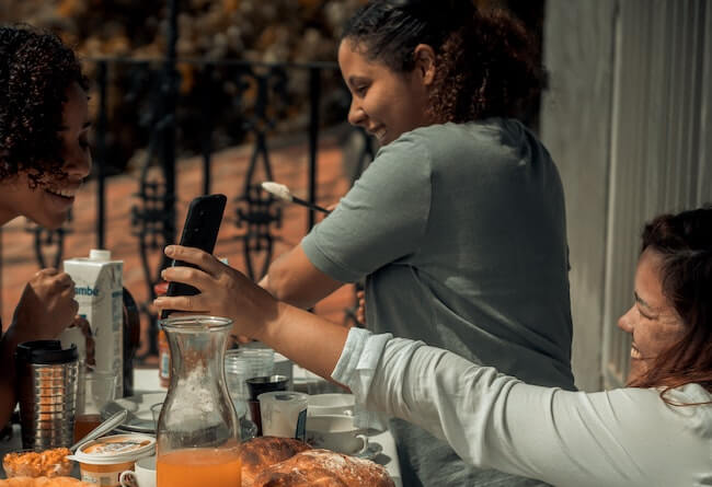 Three women laughing around a table of various breads, spreads, and beverages.