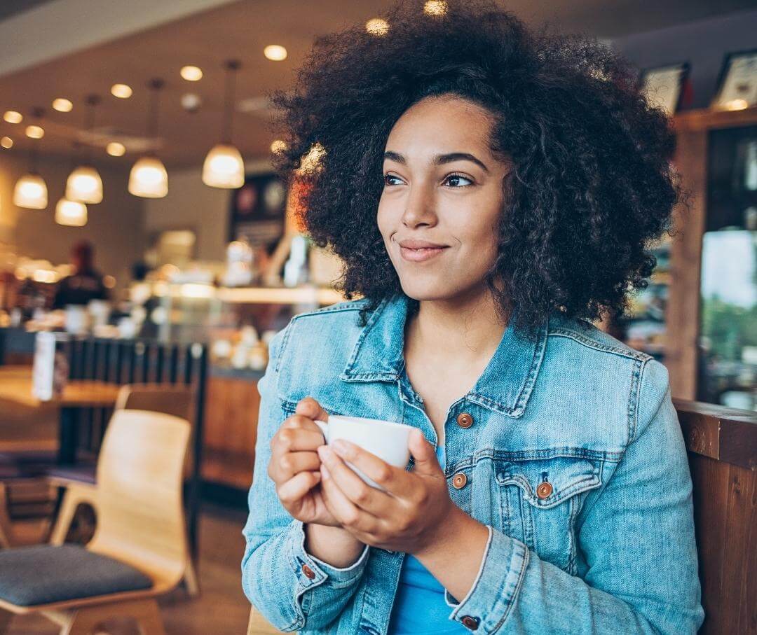 woman wearing denim jacket holding a cup of coffee in a cafe