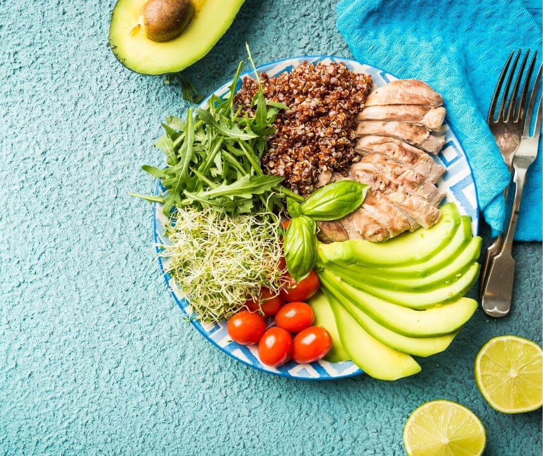 a plate with quinoa, arugula, chicken and avocado on a blue table