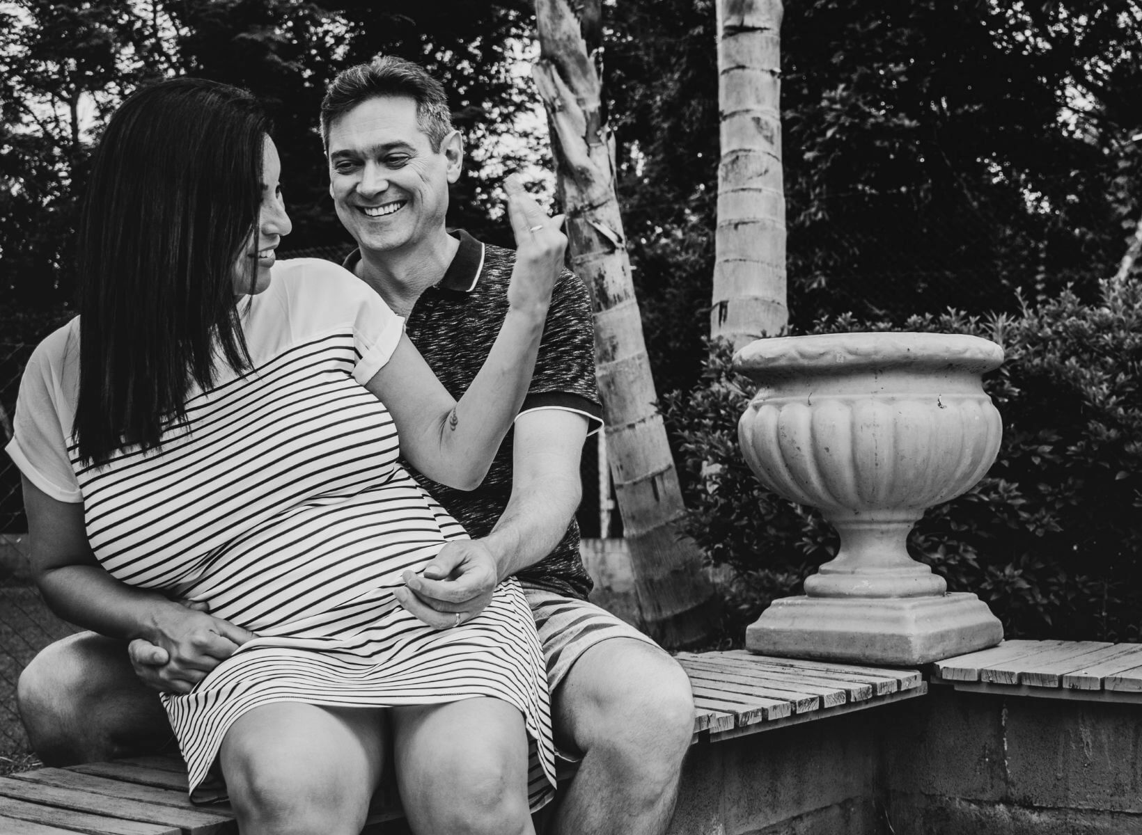 A Hispanic woman and man sitting on a bench, smiling at each other.