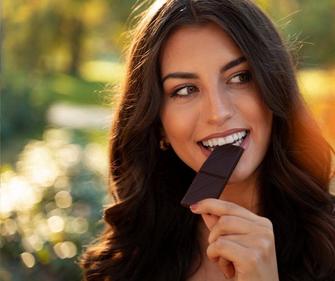 woman biting into a bar of chocolate outdoors