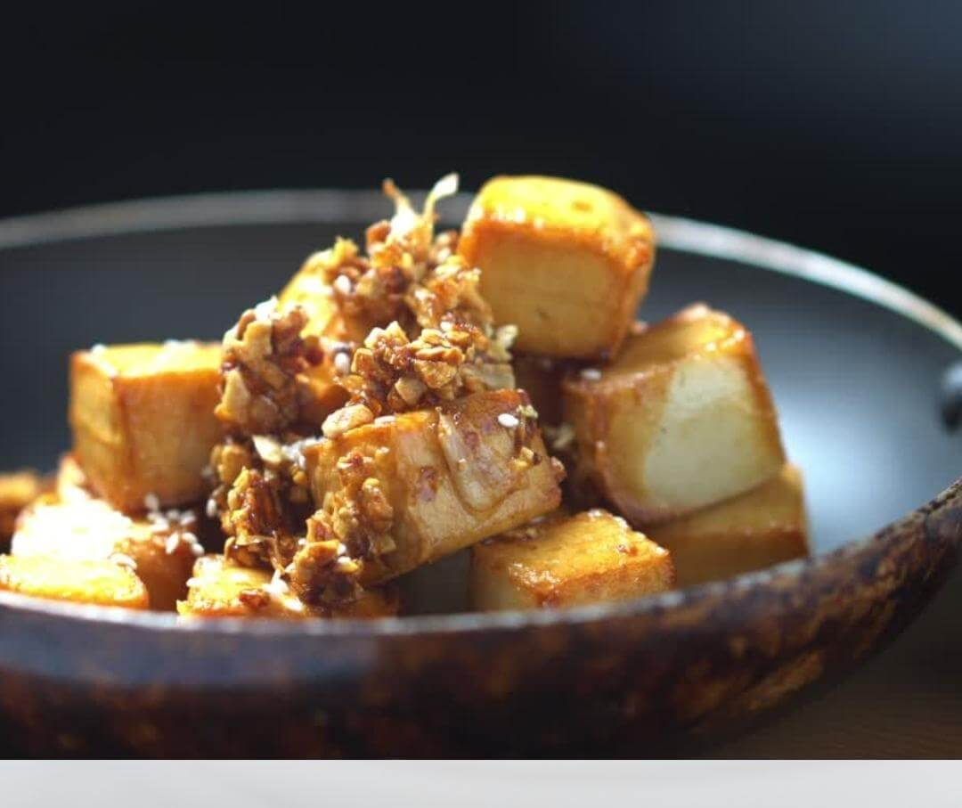 tofu pieces in a bowl with sauce and sesame seeds