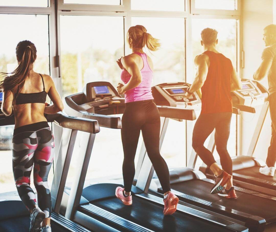 four people running on treadmills in a gym