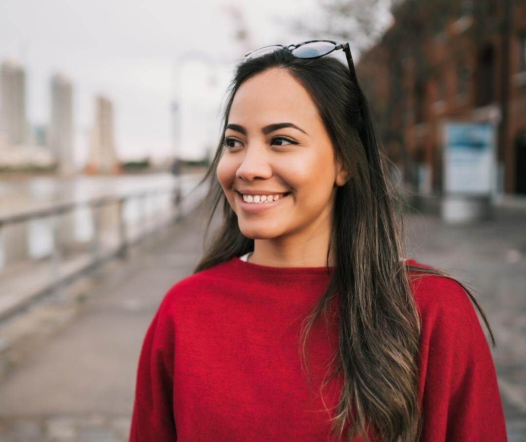 woman wearing a red sweater standing in an outdoor urban area smiling