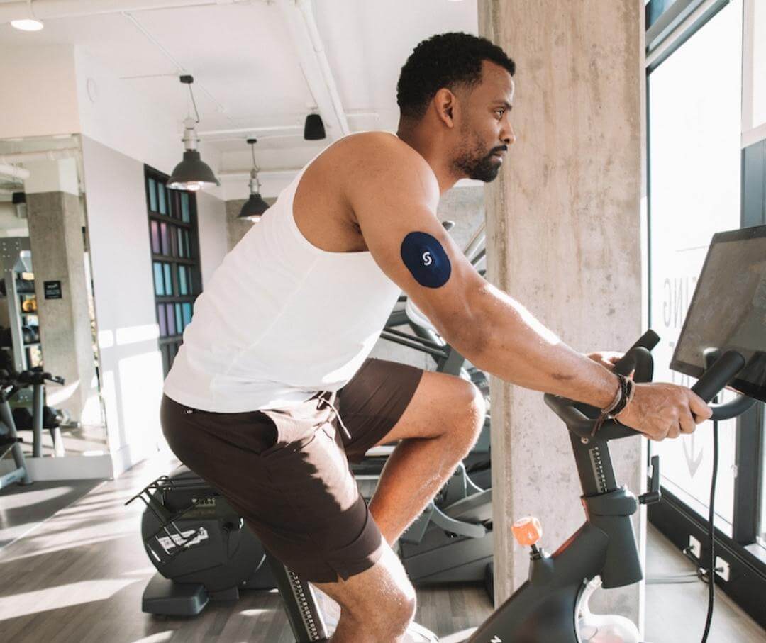 man wearing CGM riding exercise bike