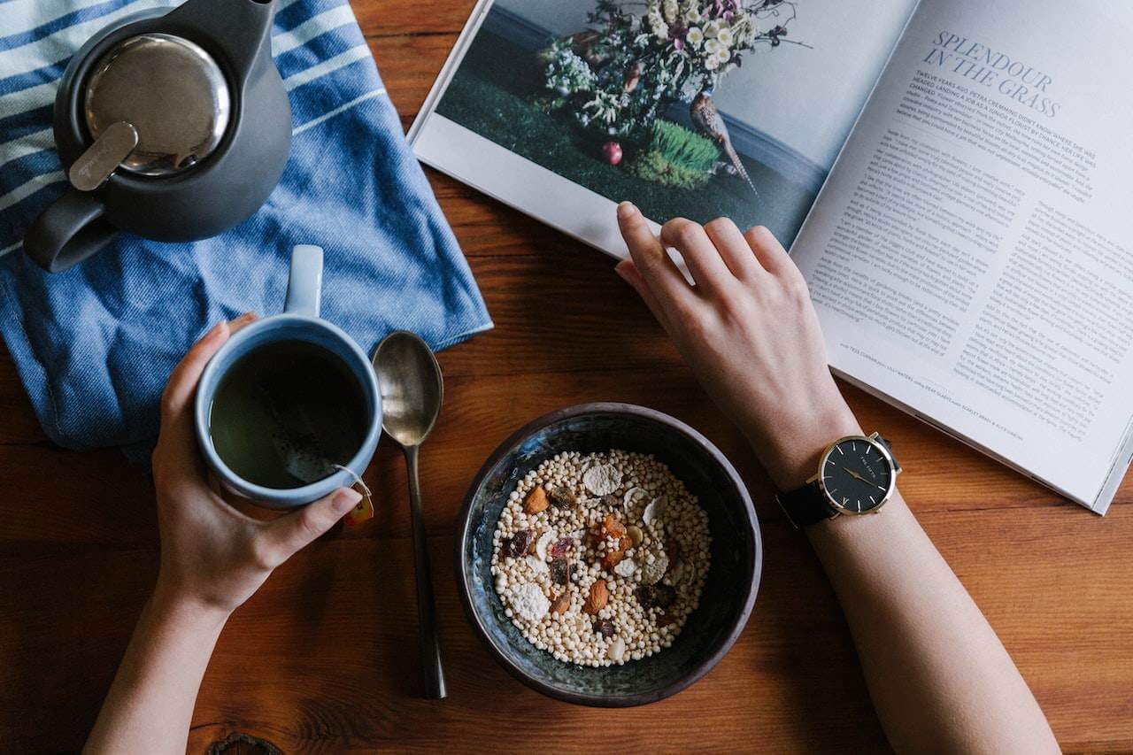 persons-hands-with-watch-eating-granola-bowl-with-coffee