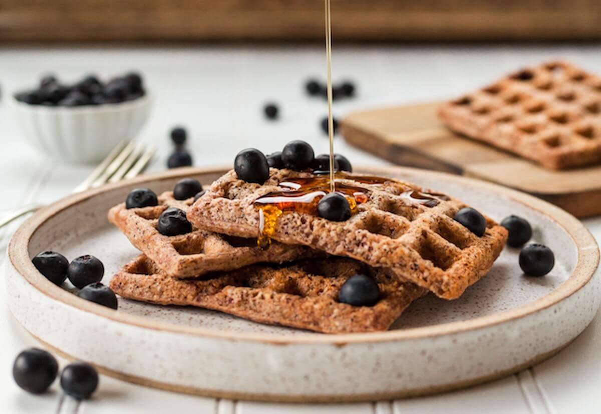 two whole grain waffles on a plate, topped with blueberries and drizzled with syrup