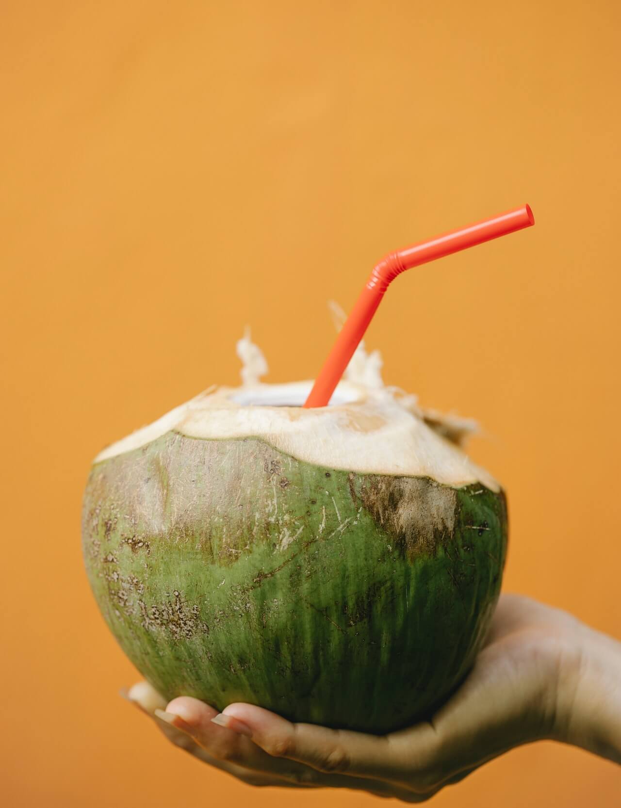 womans-hand-holding-fresh-coconut-with-its-water-and-a-straw