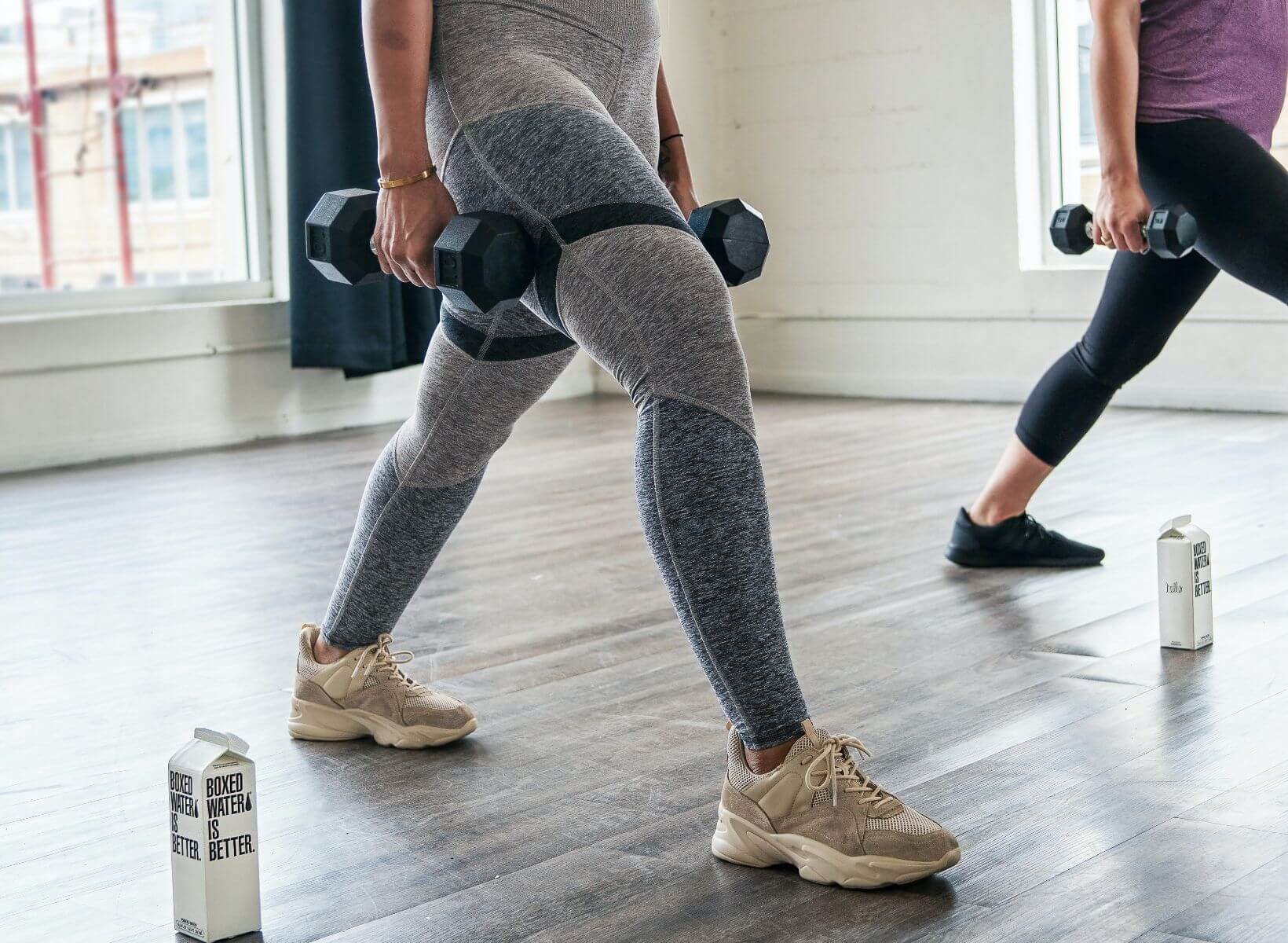 A close up shot of two women about to do weighted lunges, an exercise that can boost your metabolism