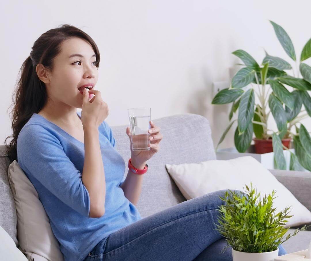 Woman taking a dietary supplement with a glass of water