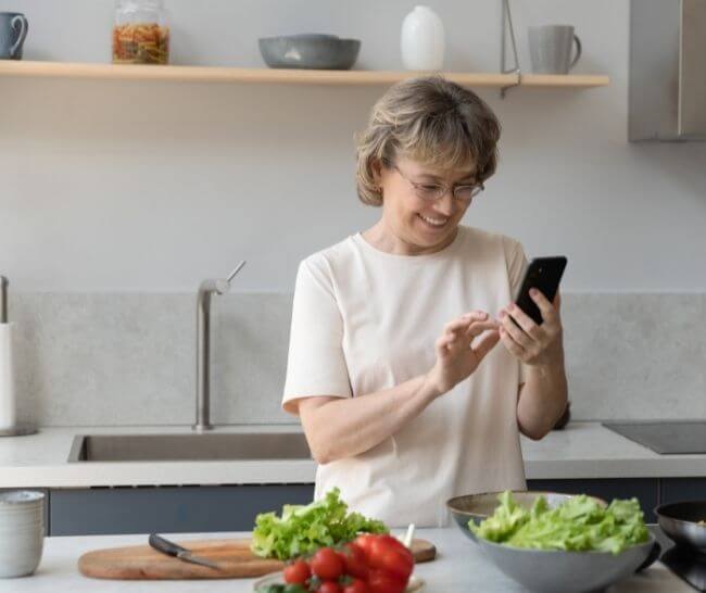 Woman smiling while looking at a recipe on her phone in the kitchen