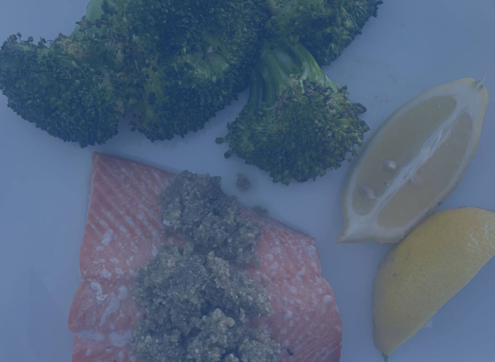 salmon with pumpkin seed pesto and roasted broccoli on a white plate with lemon wedges