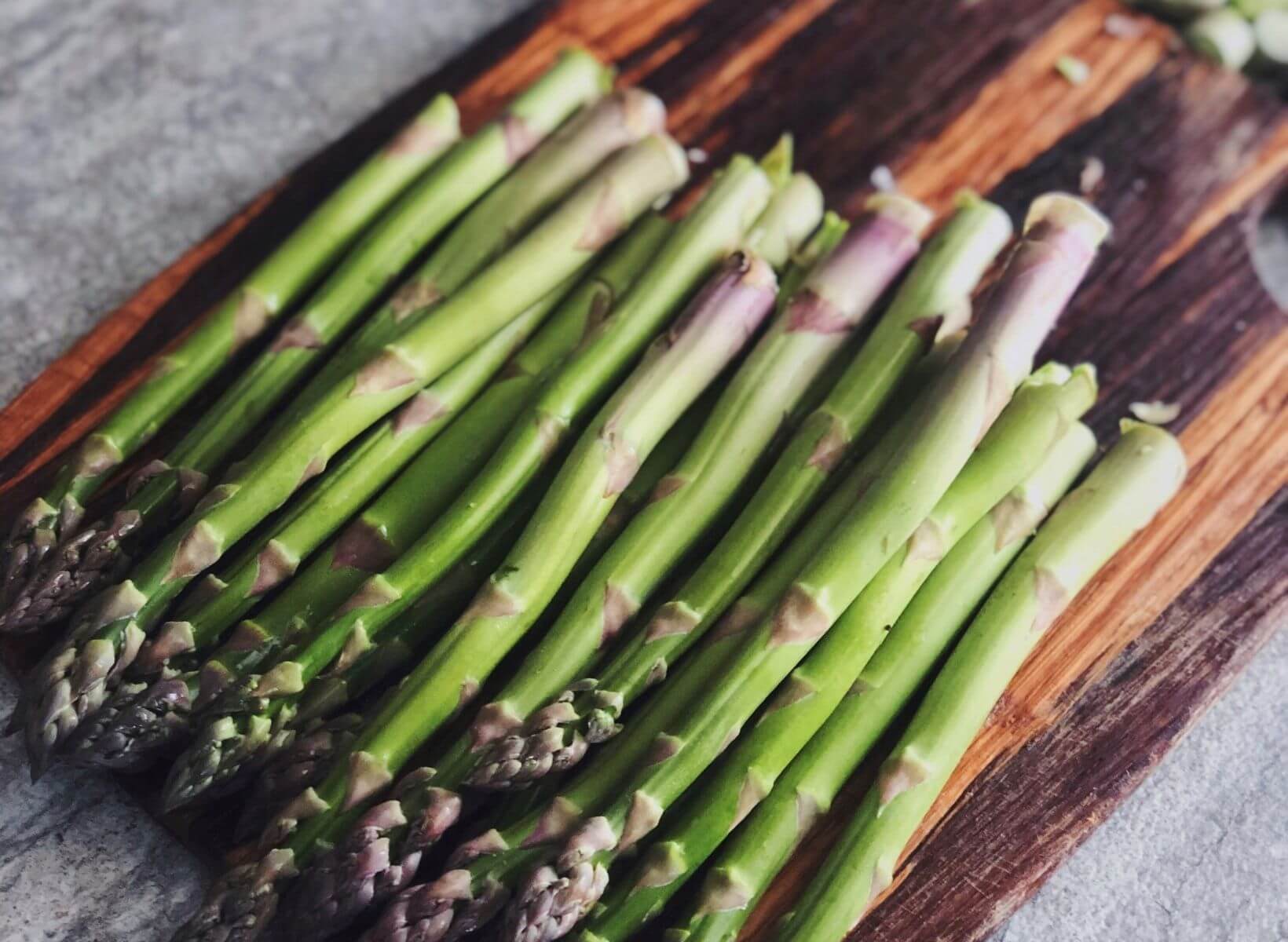 Asparagus spears, a prebiotic food, on a wood cutting board with a knife next to them