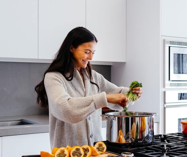 Joyful woman cooking vegetables in a stainless steel pot