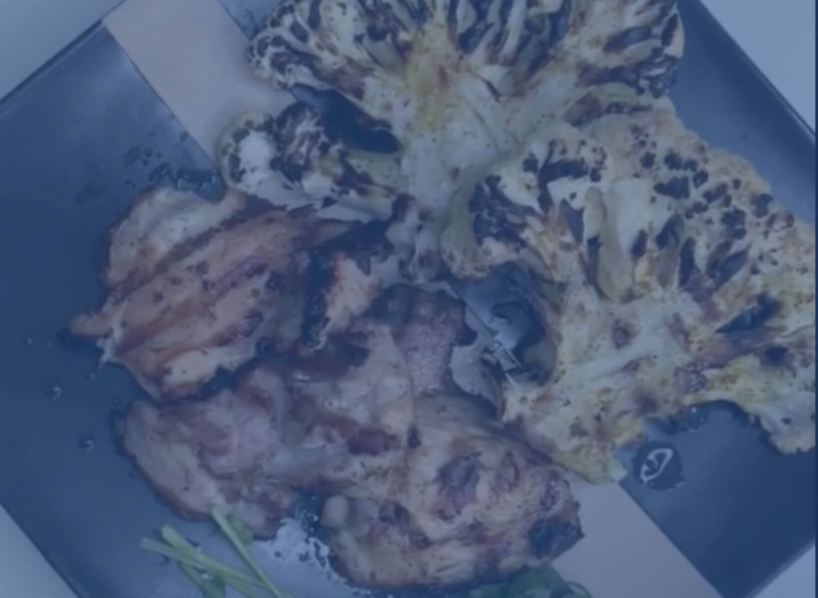 grilled chicken thighs and grilled cauliflower steaks with fresh cilantro on a black plate