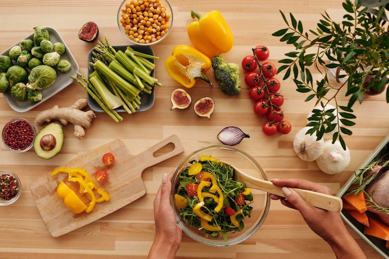 Vegetables-and-ginger-on-top-of-kitchen-counter-while-woman-prepares-a-salad