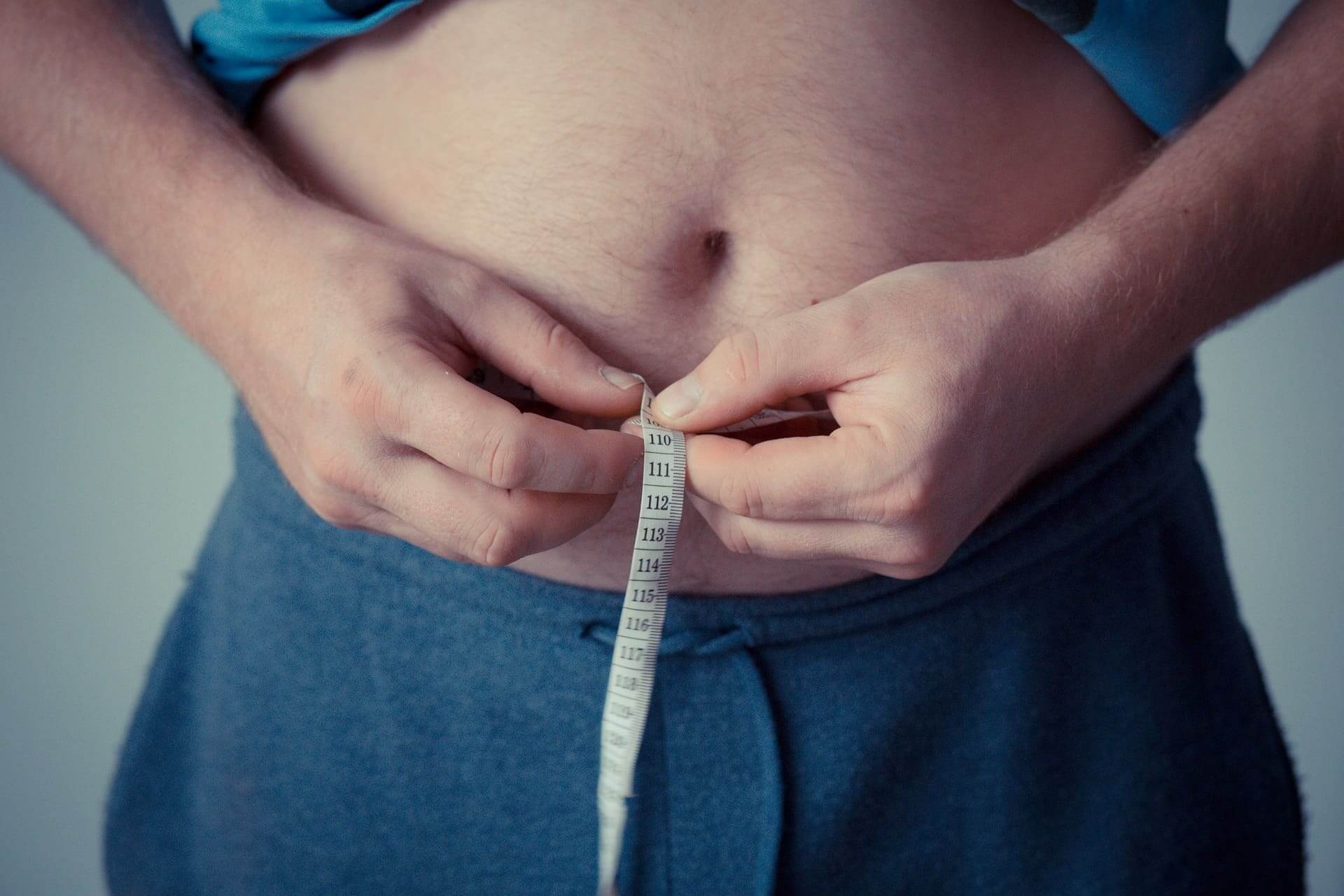 Man-holding-a-measuring-tape-against-a-bloated-stomach-foods-that-help-with-bloating