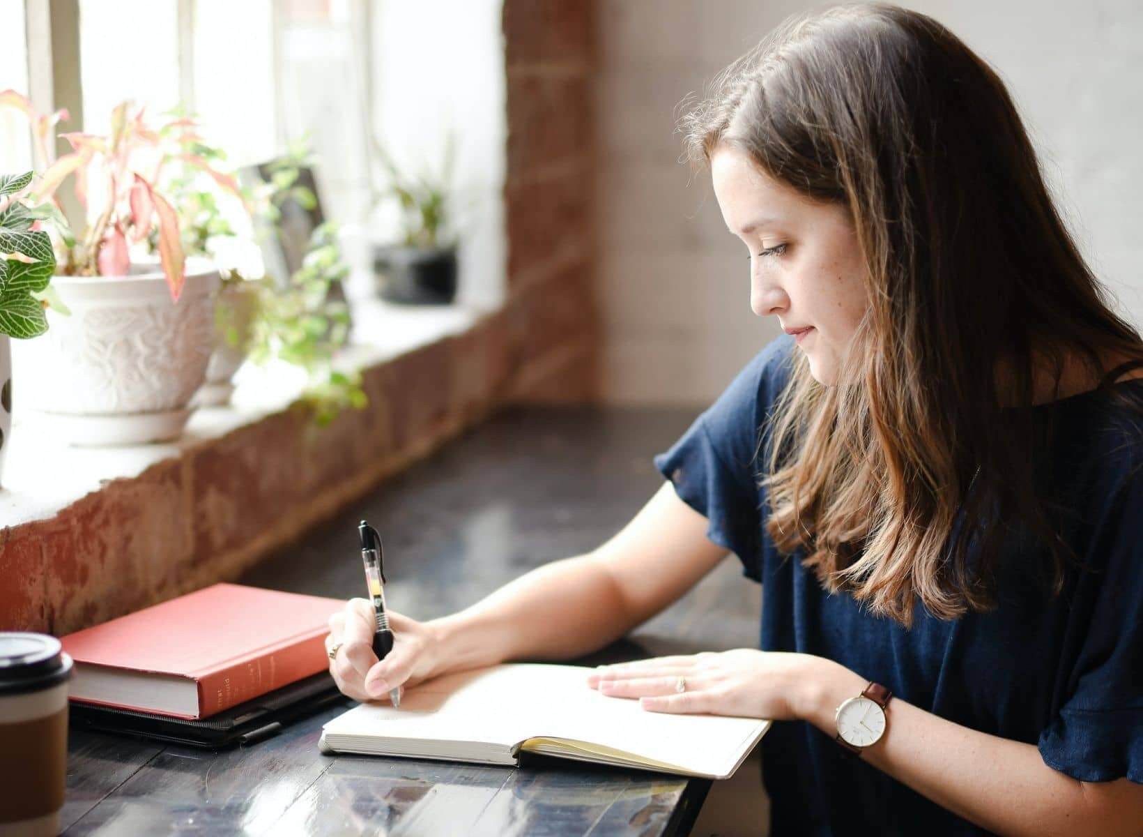 A woman sitting at a counter writing a New Year's resolution in a journal