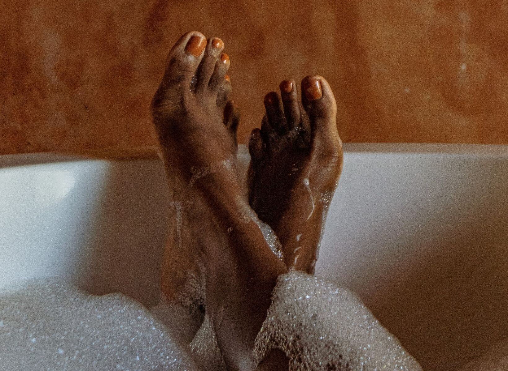 A close up shot of a woman with her ankles crossed, relaxing in a bubble bath. Taking a bath is a good way to ease holiday stress.