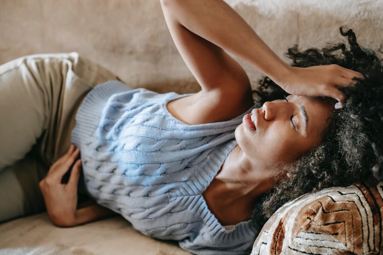 woman laying down in couch looking sick and feverish.