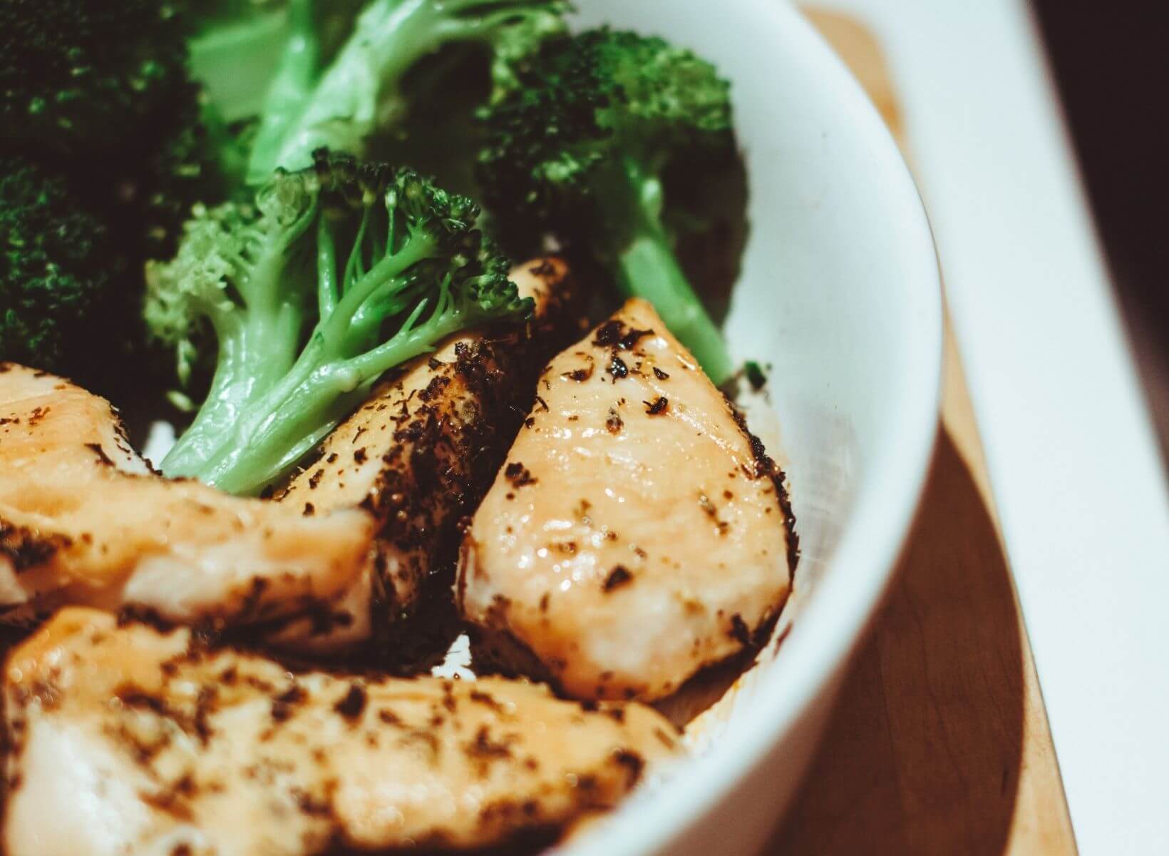 Close up shot of a white bowl that contains roasted chicken and broccoli from the chicken sheet pan dinner recipe